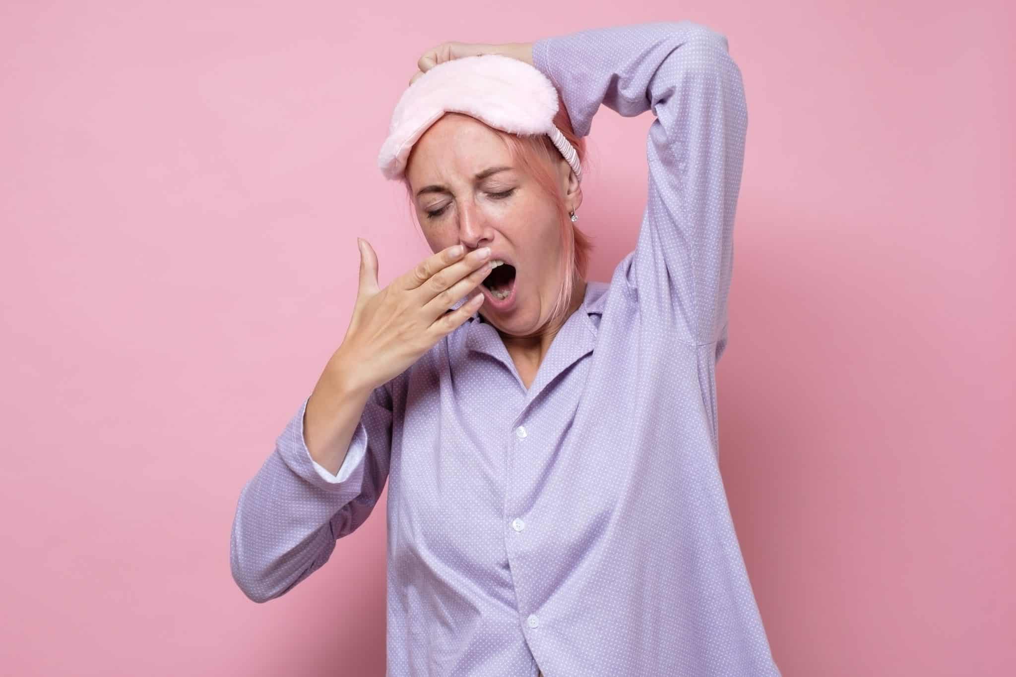 woman yawning while wearing pajamas and sleep mask
