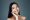 Soft sensuality. Beautiful young Asian woman looking at camera and smiling while standing against grey background