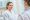 Beautiful smiling young woman in white bathrobe looking at cosmetologist in beauty clinic